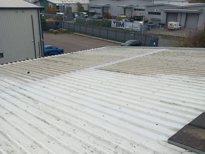 Industrial area with warehouses and parked cars behind a corrugated metal roof.