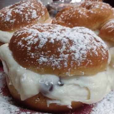 Powdered sugar-covered stuffed donuts arranged on a white plate.