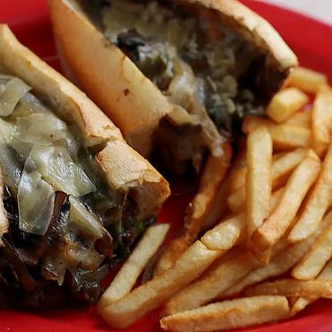 A delicious cheesesteak with melted cheese served on a plate, alongside a generous portion of golden