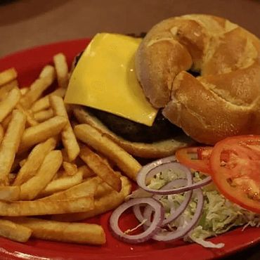 A red plate featuring a juicy hamburger with toppings and a side of golden French fries