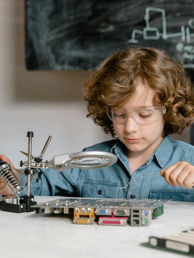 A child wearing safety glasses soldering an electronic circuit board.