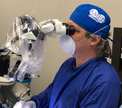 A medical professional uses a microscope during a procedure.
