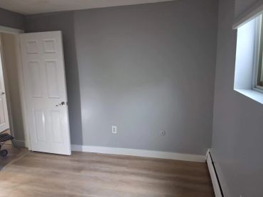 Empty room with gray walls, light wood floor, and open door.