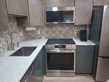 Modern L-shaped kitchen with stainless steel appliances and floral tile backsplash.