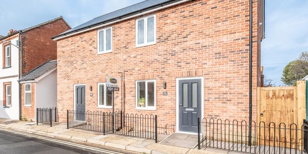 Modern brick house with dark doors and a 'For Sale' sign on a sunny day.