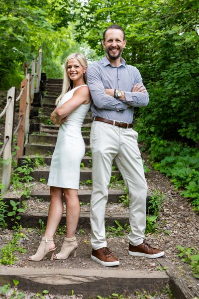 Smiling man and woman standing back-to-back outdoors by stairs.