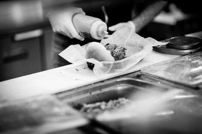 A person preparing a sandwich with sauce in a kitchen setting.