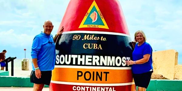 Two people pose at the Southernmost Point buoy in Key West, Florida.
