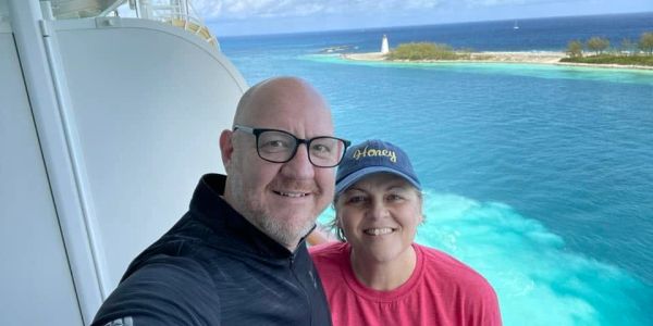 Couple smiling on a cruise balcony with a scenic ocean view.