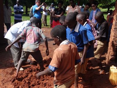 Children playing and interacting in muddy ground outdoors.