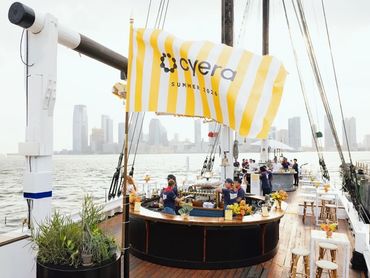 People enjoying a drinks bar on a boat with city skyline in background.