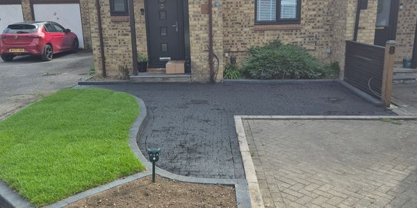 Newly paved driveway with adjacent green lawn and a brick house entrance.