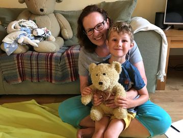 Mother and young child sitting floor in a living room smiling. Child holding teddy bear