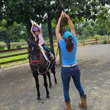 Child on a pony mimicking an Instructor with arms raised above their head