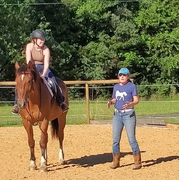 Woman sitting on a standing horse, listening to an instructor standing next to them