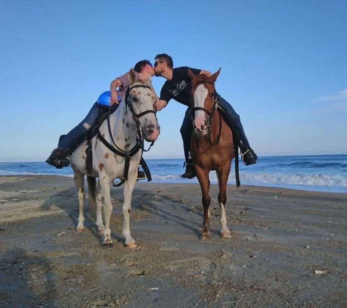Man and woman on horseback kissing on a beach