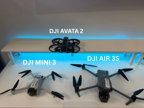 Three DJI drones displayed on a white table with blue backlight.