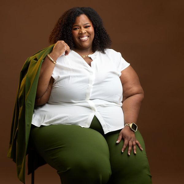 Confident woman smiling, sitting against brown background.