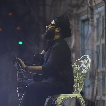 Bearded man playing guitar on a decorative chair.