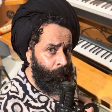 Man with beard and turban singing into microphone.