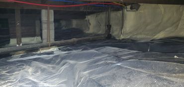 Crawl space with plastic ground cover and pipes.
