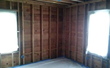 A room with exposed wooden studs and covered windows.