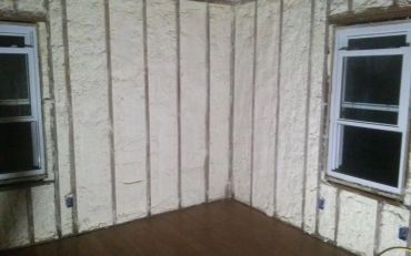 Room with spray foam insulation on walls and two windows.