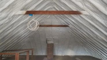 Attic with spray foam insulation and wooden beams.