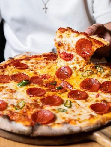Hand lifting a slice of pepperoni pizza with melted cheese and jalapeños.