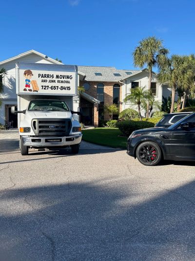 Moving truck and black SUV outside a home with palm trees.