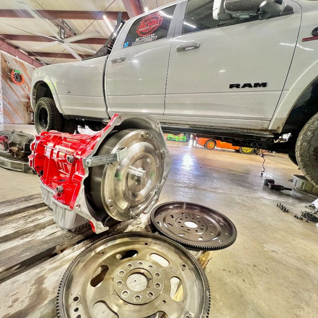 A white RAM truck in a garage with a red transmission and parts on the floor.