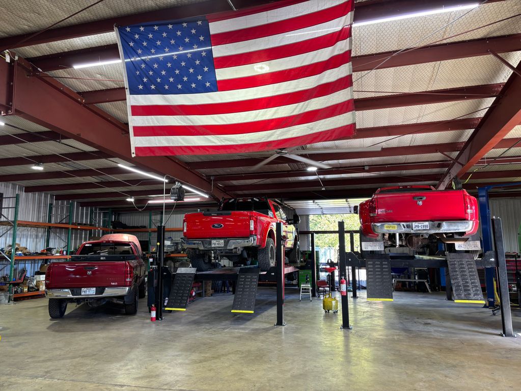 Three red pickup trucks inside a spacious garage with an American flag overhead.