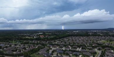 Lightning striking in the distance over a suburban neighborhood under a cloudy sky.