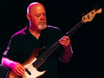 A man playing an electric bass guitar on stage with focused expression.