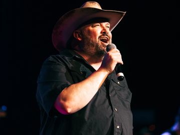 A man in a cowboy hat singing into a microphone on stage.