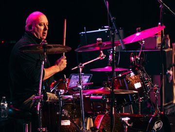 Man playing drums on stage during a live performance.