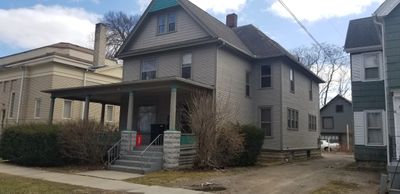 A two-story gray house with a covered porch and bushes in front.