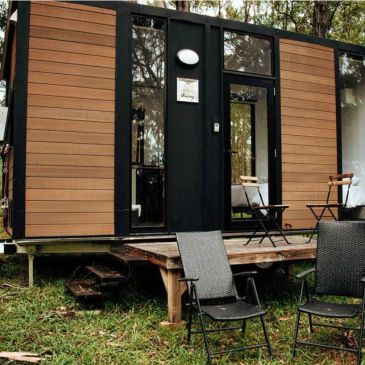 Modern tiny house with wooden accents and outdoor seating in a forest setting.