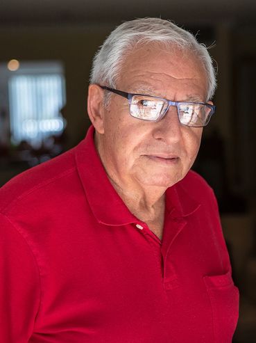 A 97 year old man wearing a red polo with glasses on.