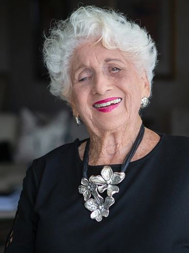 A 99 year old woman from the Holocaust smiling wearing pink lipstick and a black blouse