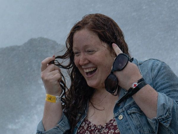 A joyful woman enjoying a moment near water, holding sunglasses.