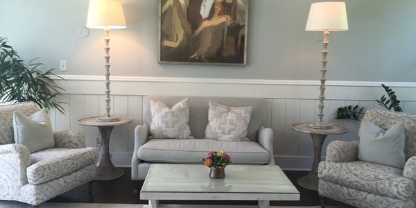 a gray couch, two chairs, a coffee table w/ small flower arrangement, art above the centered couch