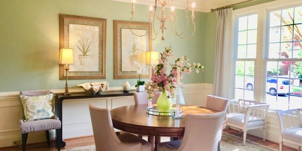 Dining room with round table with a flower arrangement, chairs, green paint on the wall, side table.