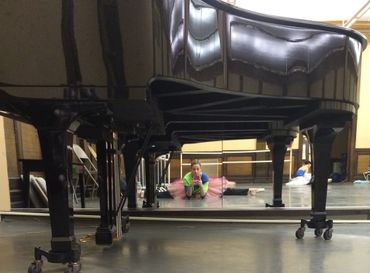 Ballerina in a pink tutu stretching and taking a selfie under a grand piano.