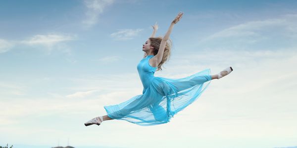 A ballet dancer in a flowing blue dress leaps gracefully against a cityscape.