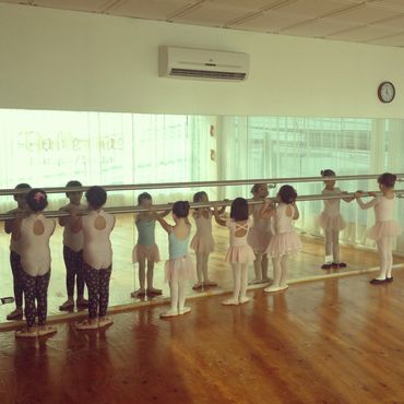 Young children practicing ballet at a dance studio barre.
