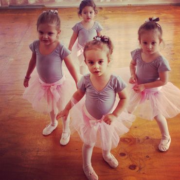 Four young girls in ballet outfits standing on a wooden floor.