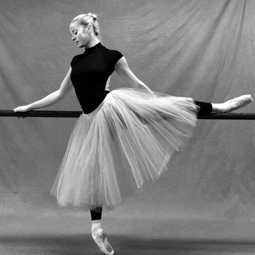 Ballerina in pointe shoes practicing at the barre in a flowing tulle skirt.