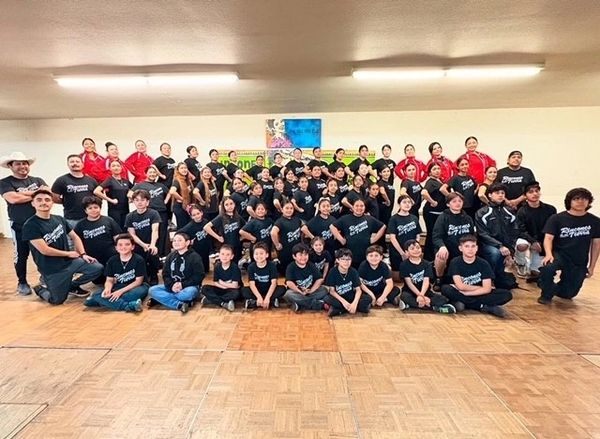 Large group of young dancers posing indoors, some in black shirts and others in red outfits.