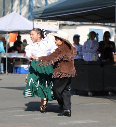 Two children in traditional attire performing a folk dance outdoors.